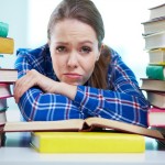 Portrait of a frustrated student being surrounded with piles of books